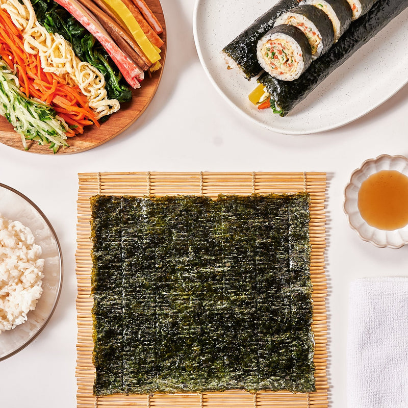 Seaweed sheet on a bamboo mat with gimbap fillings, rice and sliced gimbap