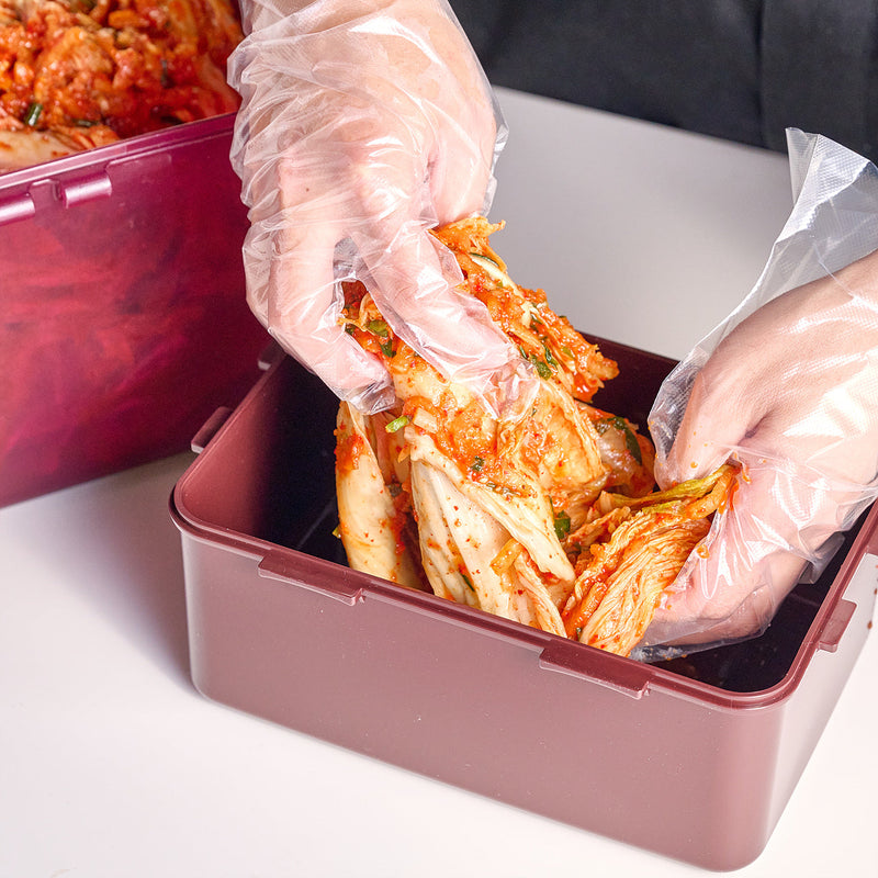 Gloved hands packing napa cabbage kimchi into a storage container
