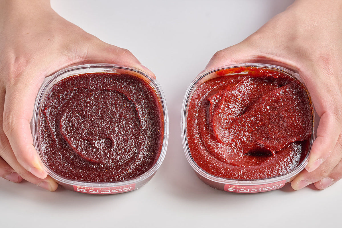 Two containers of gochujang side by side showing a darker and a brighter red color