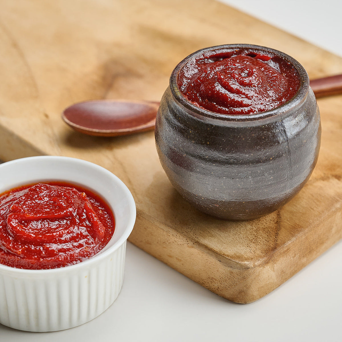 Gochujang in a ceramic jar and a small white bowl on a wooden board